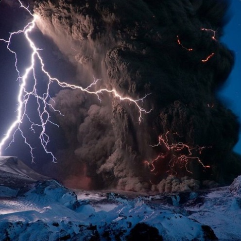 Volcanic lightning flashing through a towering ash cloud at night.