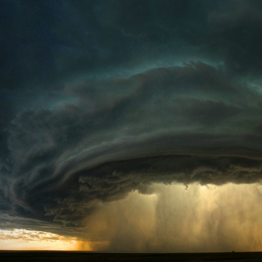 A supercell thunderstorm glowing gold above a dark horizon.